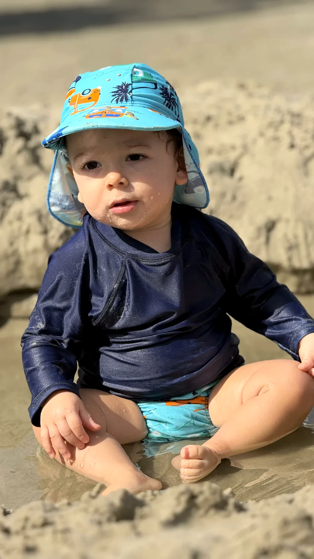 Bebê com roupa e chapéu Pulpo descobrindo a água na beira da praia